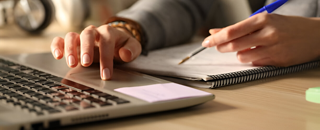 Persona en su computadora tomando apuntes en un cuaderno